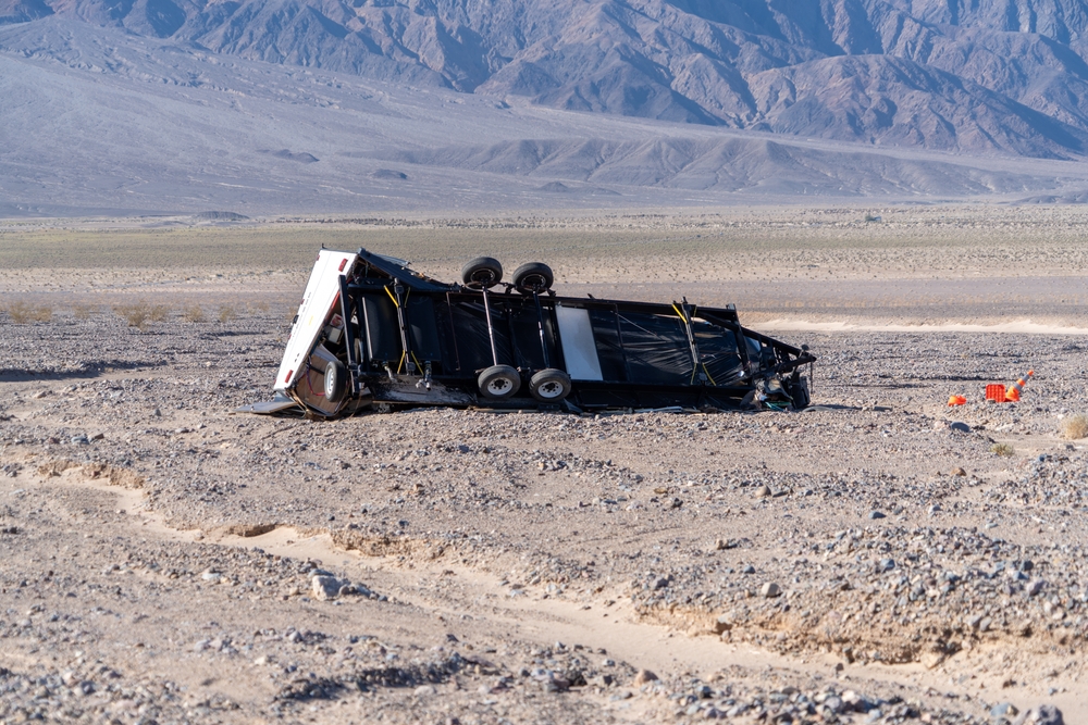 Towable RV crashed and on its side in a deserted area.